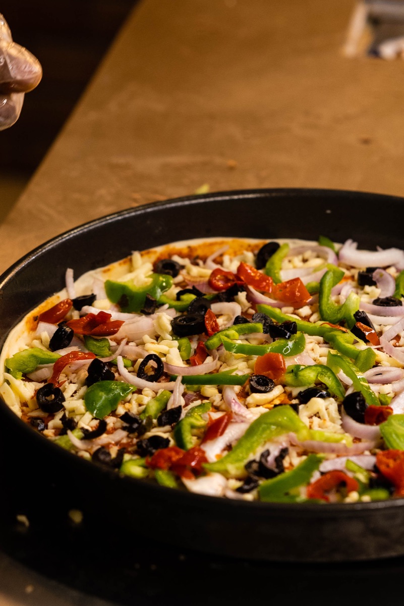 Pizza being topped by hand in the open kitchen